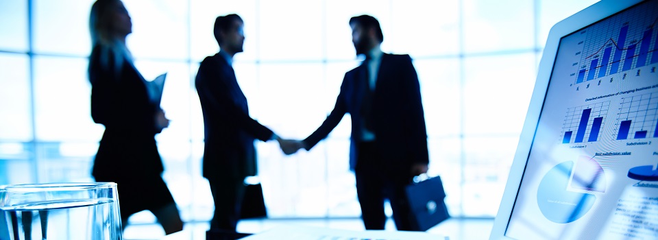 Laptop, financial document with pen and glass of water at workplace on background of three business partners making a deal